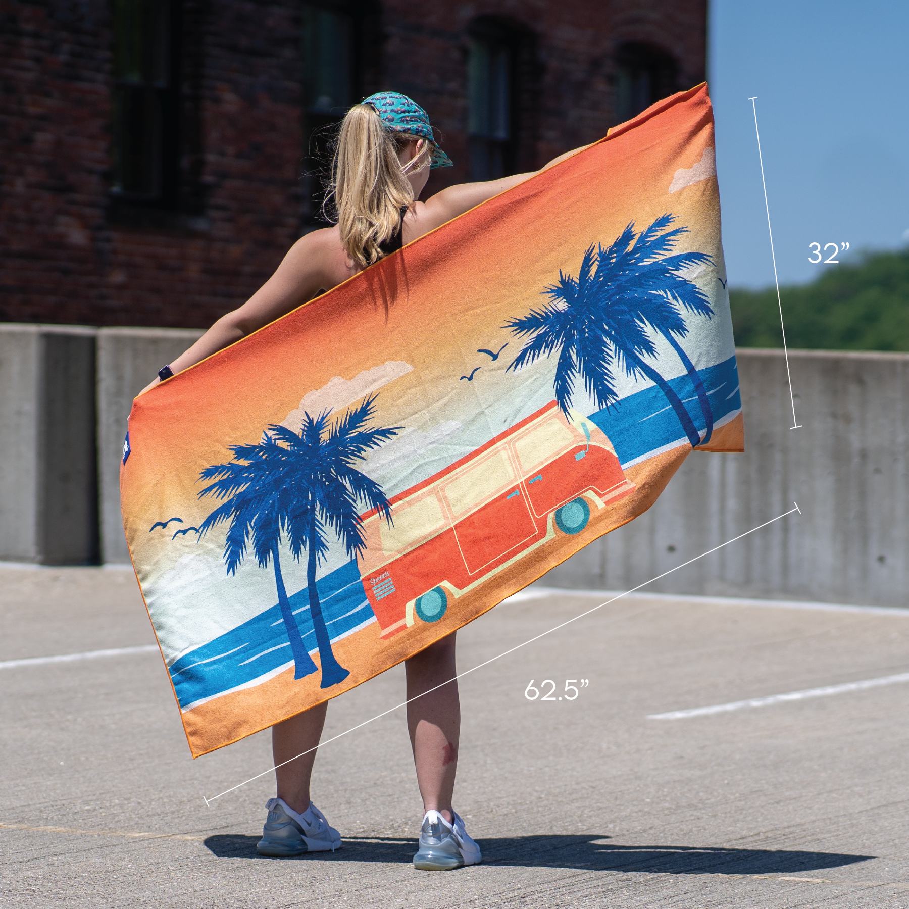 Image of towel with van in front of sunset near trees. Color is orange and blue. Shows size of 62.5 inches by 32 inches.