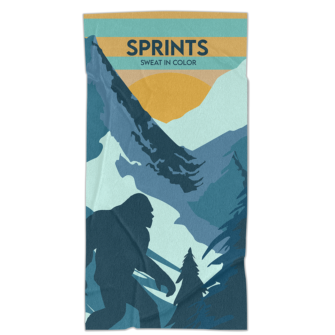 Towel with image of Sasquatch character against mountains and tress in blue and orange and teal color.