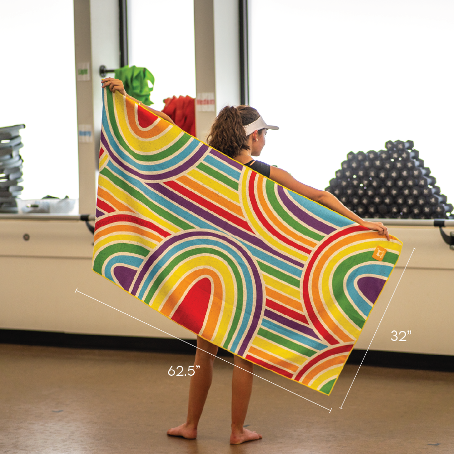 Woman showing a 62.5 inch by 32 inch towel with multi-color rainbows