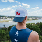 Person wearing a cap with 'USA' and a sleeveless shirt with stars, overlooking a scenic landscape.