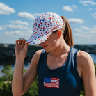 Woman wearing a blue tank top with an American flag and a patterned cap outdoors.