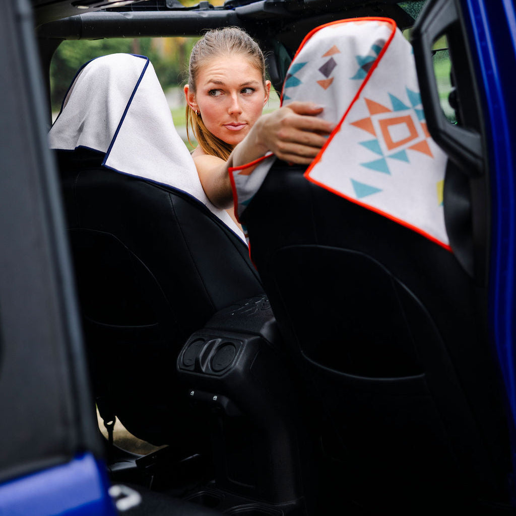 Person holding a colorful patterned pillow inside a vehicle with trees in the background
