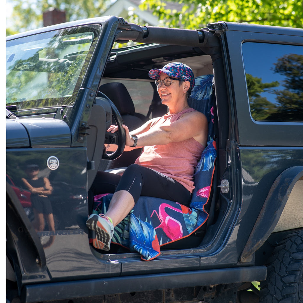 Towel with pattern of pink flamingos against tropical leaves in dark blue and green background on driver seat of jeep.