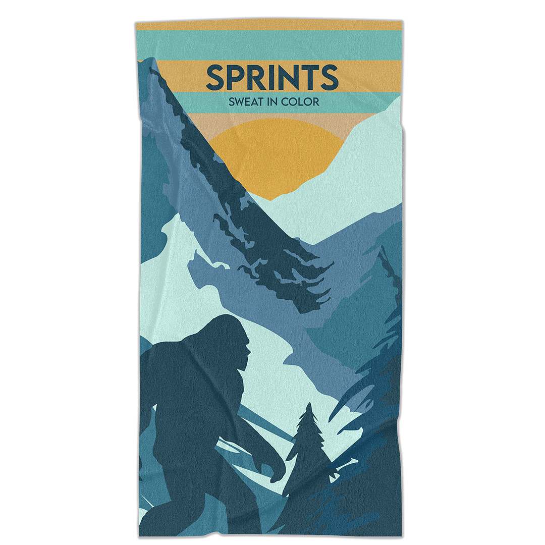 Towel with image of Sasquatch character against mountains and tress in blue and orange and teal color. 