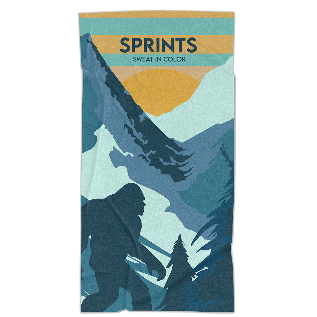 Towel with image of Sasquatch character against mountains and tress in blue and orange and teal color. 